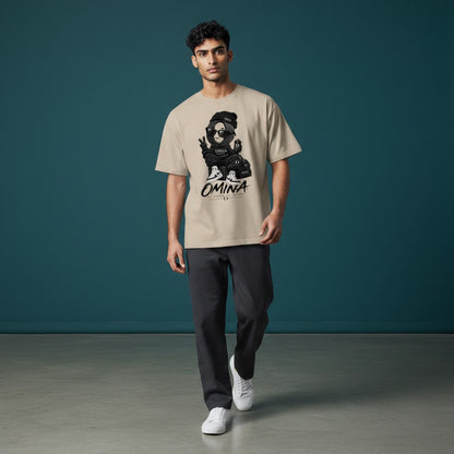 Model wearing an Omina O Urban beige cotton t-shirt with a graphic print, styled with dark trousers and white sneakers.