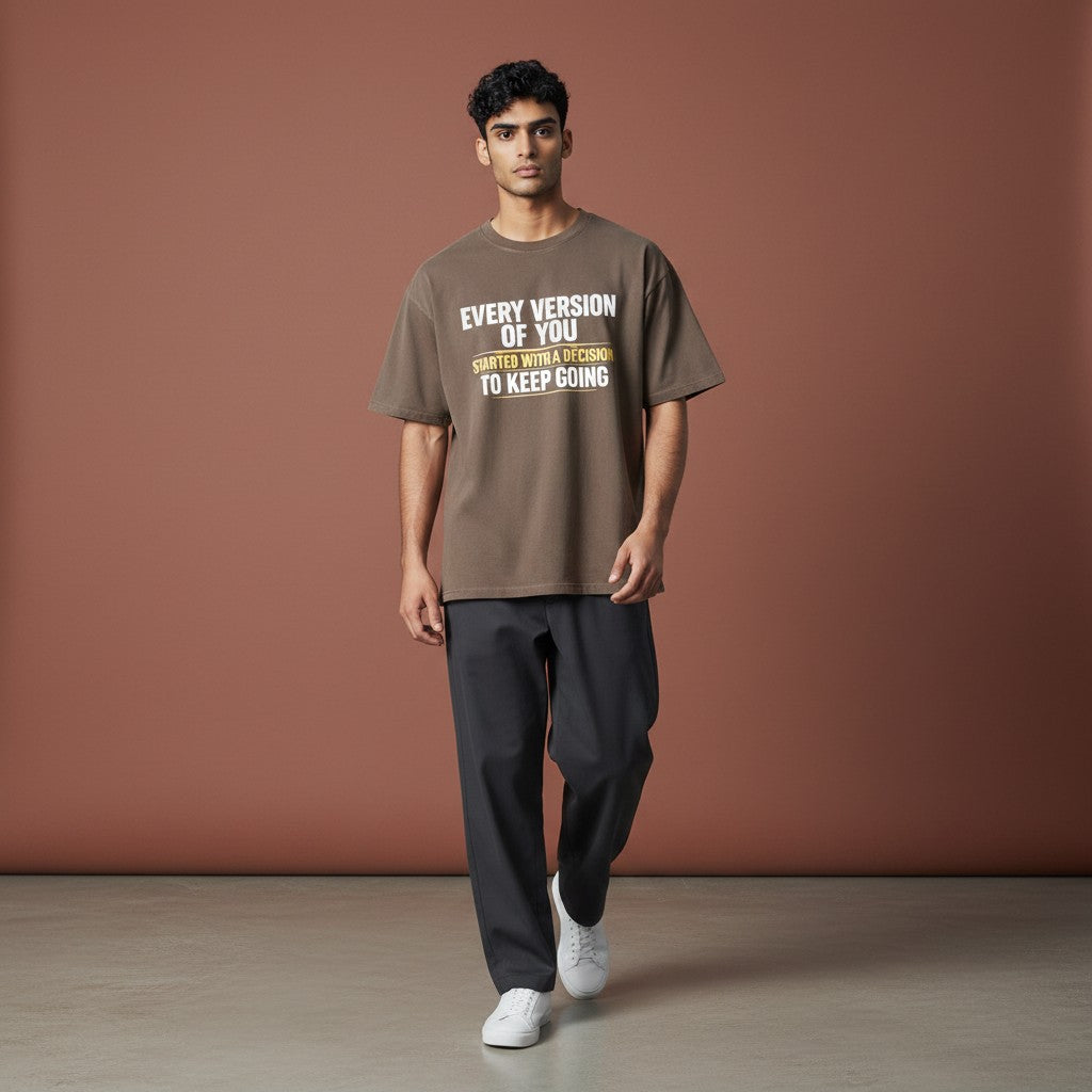 Omina taupe 100% cotton unisex vintage wash boxy t-shirt with a round neck and drop shoulders, featuring white text that reads "EVERY VERSION OF YOU STARTED WITH A DECISION TO KEEP GOING".