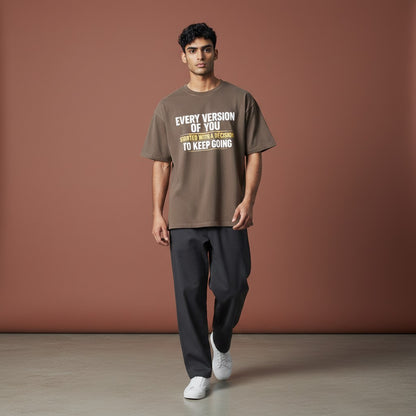 Omina taupe 100% cotton unisex vintage wash boxy t-shirt with a round neck and drop shoulders, featuring white text that reads "EVERY VERSION OF YOU STARTED WITH A DECISION TO KEEP GOING".