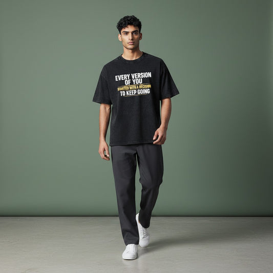 Omina black vintage wash 100% cotton unisex t-shirt with a loose fit, drop shoulders, and round neck. Features white text that reads "EVERY VERSION OF YOU STARTED WITH A DECISION TO KEEP GOING".