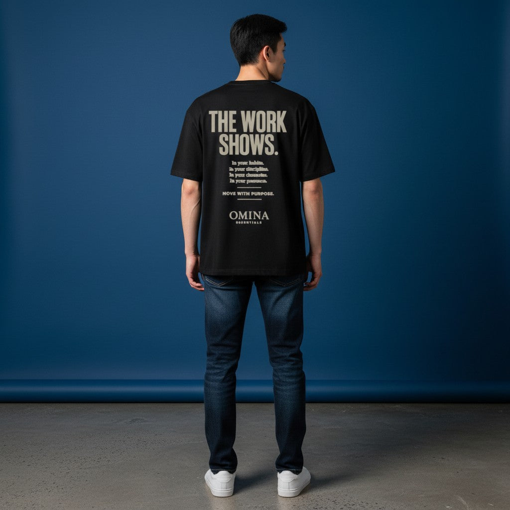 Omina black cotton t-shirt with "THE WORK SHOWS." graphic print on back. Model is wearing jeans.