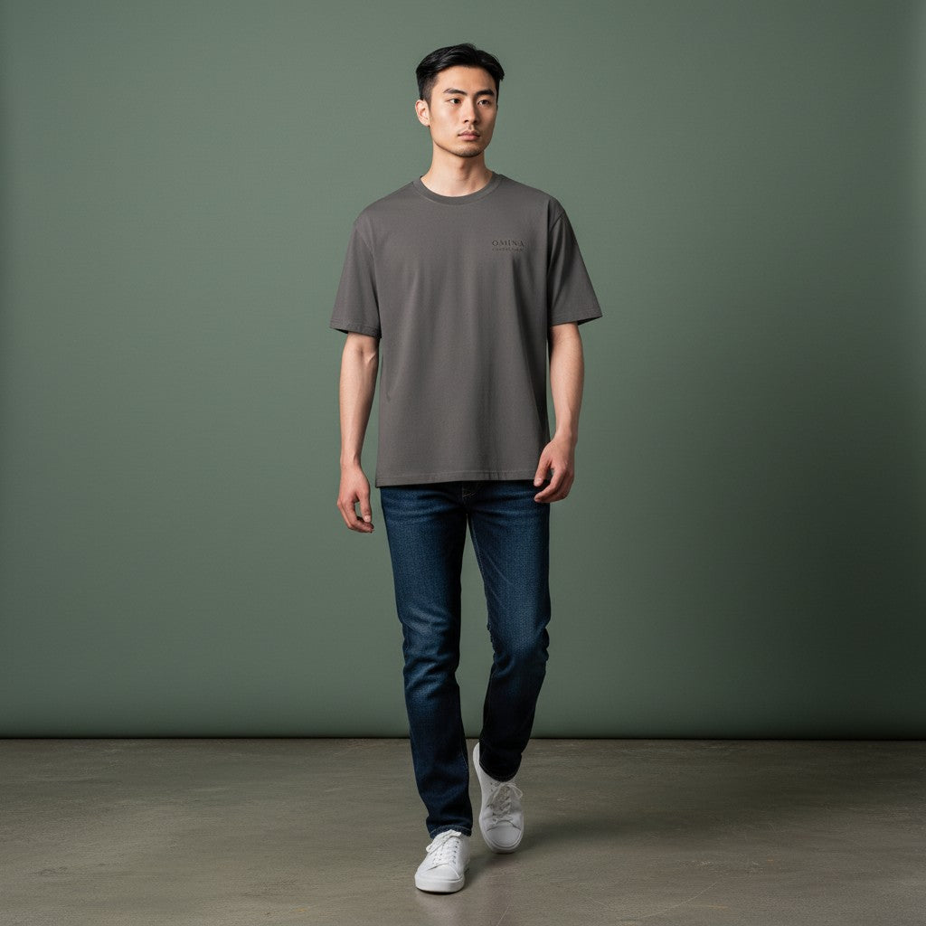 Omina charcoal grey cotton t-shirt with minimalist logo detail on chest, worn by a man with dark jeans.