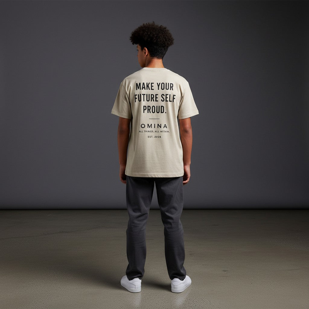 Youth wearing Omina beige performance tee with Future Self Proud text on back, standing against grey background.