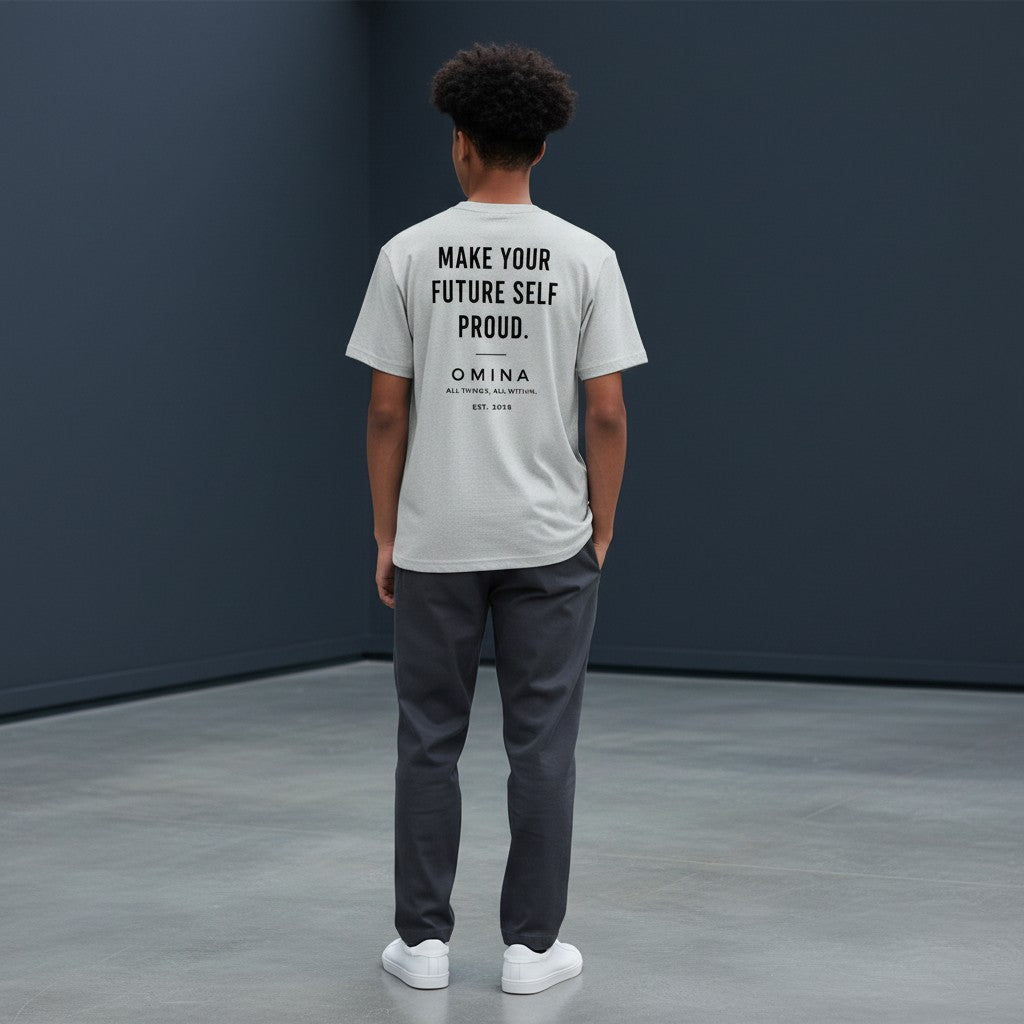A youth wearing a grey Omina performance tee with Future Self Proud text on the back, standing in a studio.